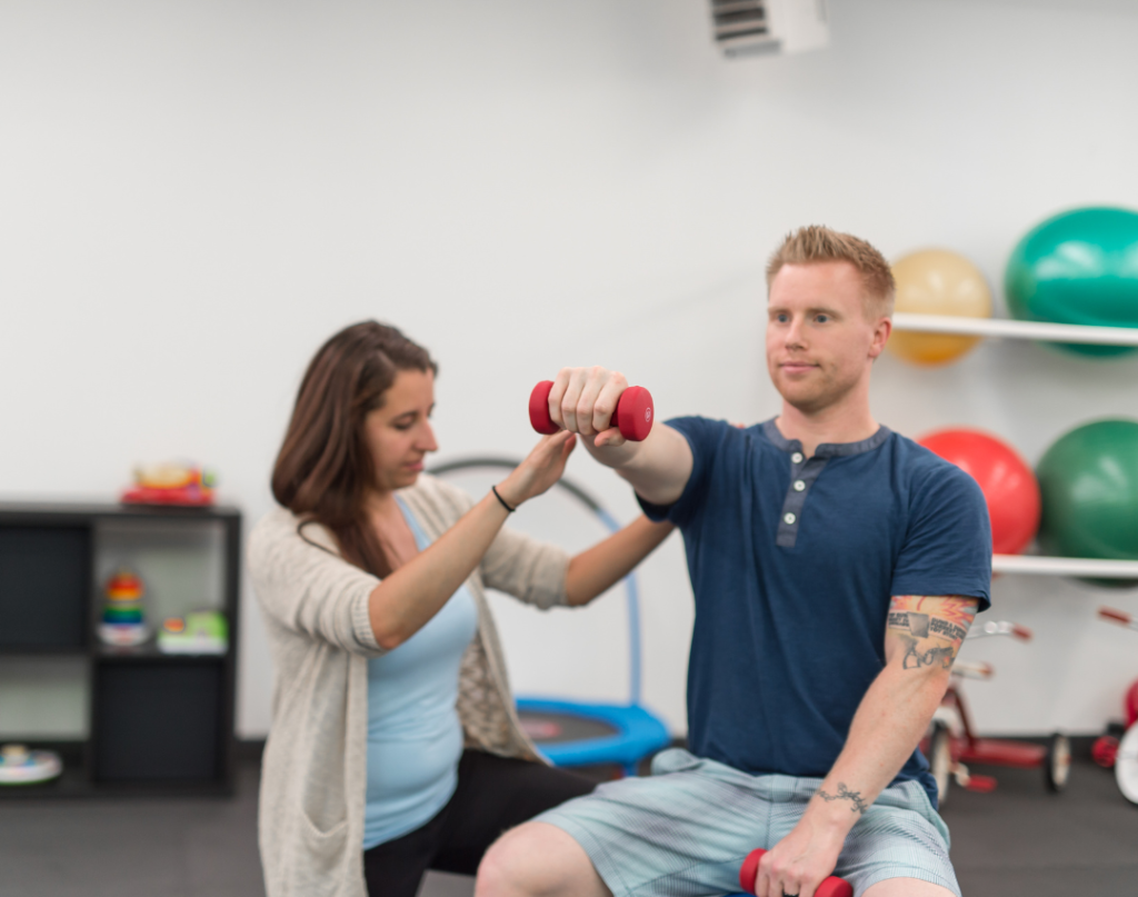 A man lifting a small dumbbell while a physical therapist guides his movement
